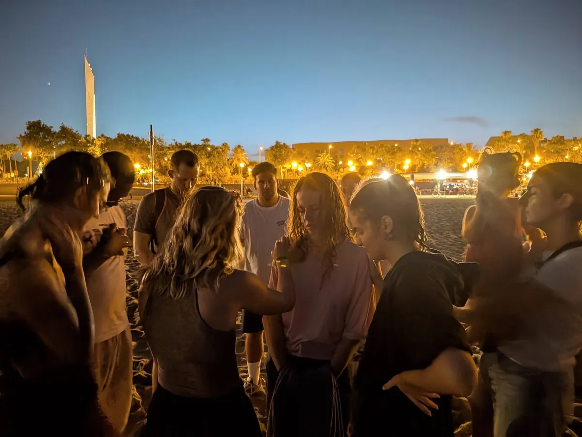 A group praying together on a Barcelona beach at dusk