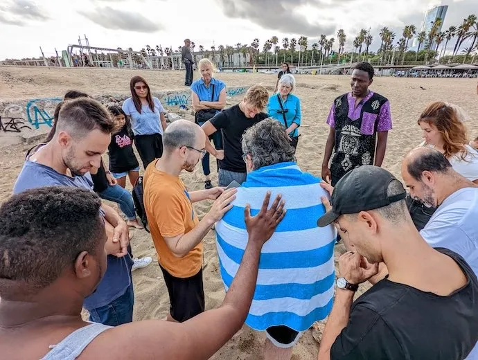 Believers praying over a man on the beach in Barcelona